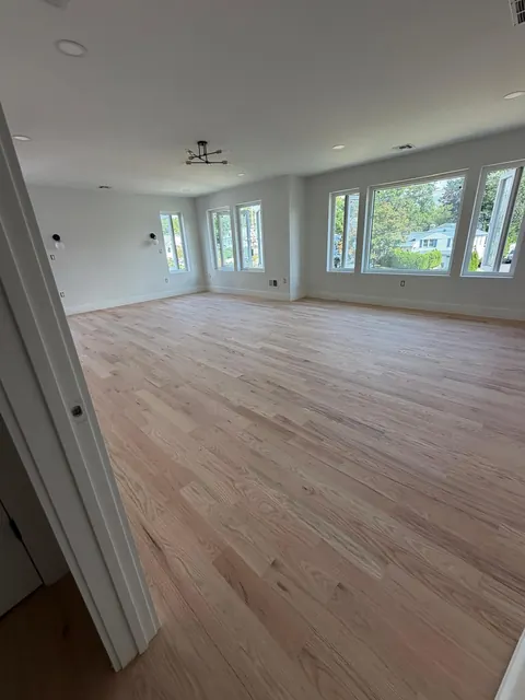 Large sunlit room with a natural-finish oak floor and a wall of windows