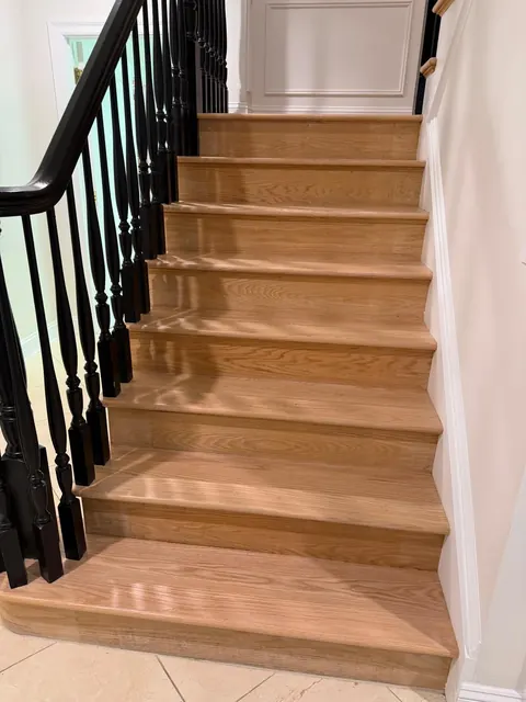 Staircase with light oak treads and black balusters, white wainscoting