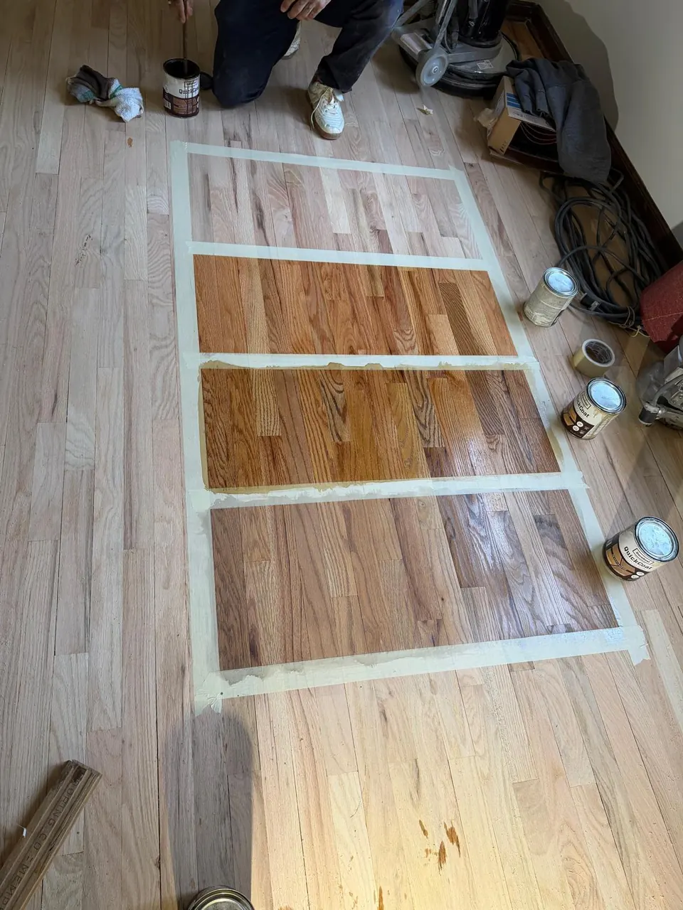 Four stain colors taped out as samples on a sanded oak floor